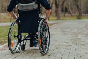 Close-up of male hand on wheel of wheelchair during walk in park. He holds his hands on the wheel.