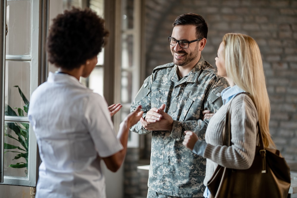 Happy army soldier and his wife communicating with healthcare worker for a veterans disability claim