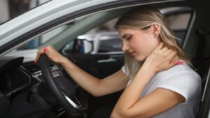 Young woman suffering from neck whiplash personal injury, sitting in drivers seat of her car