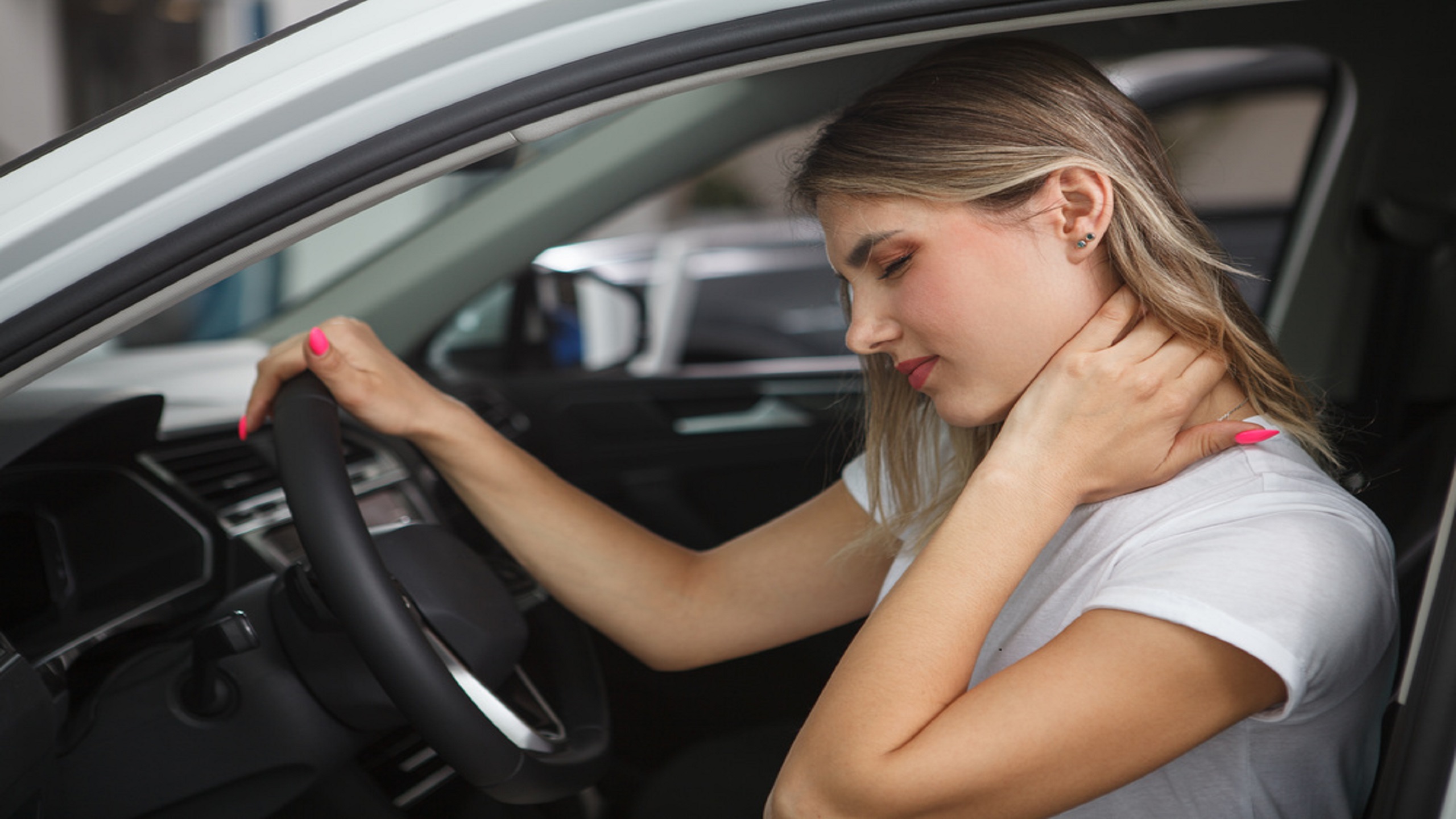 Young woman suffering from neck whiplash personal injury, sitting in drivers seat of her car