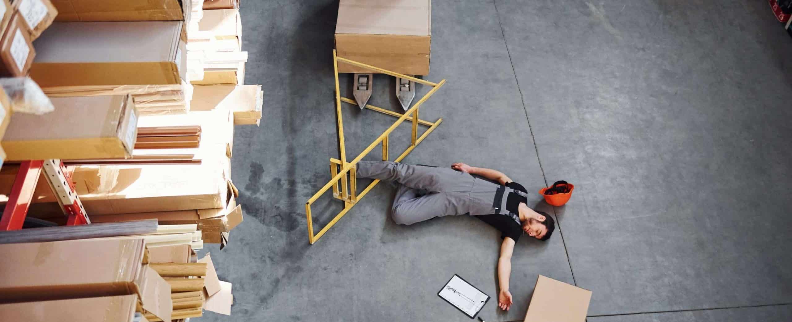Warehouse worker after an accident in the storage. Man in uniform lying down on the ground.